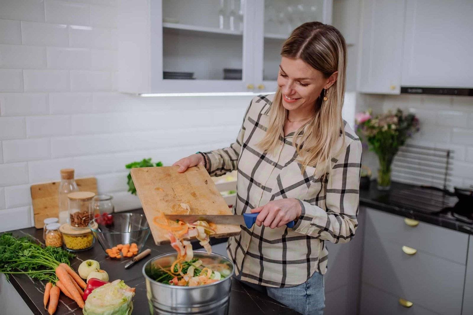 Woman throwing vegetable cuttings in a compost bucket in kitchen.